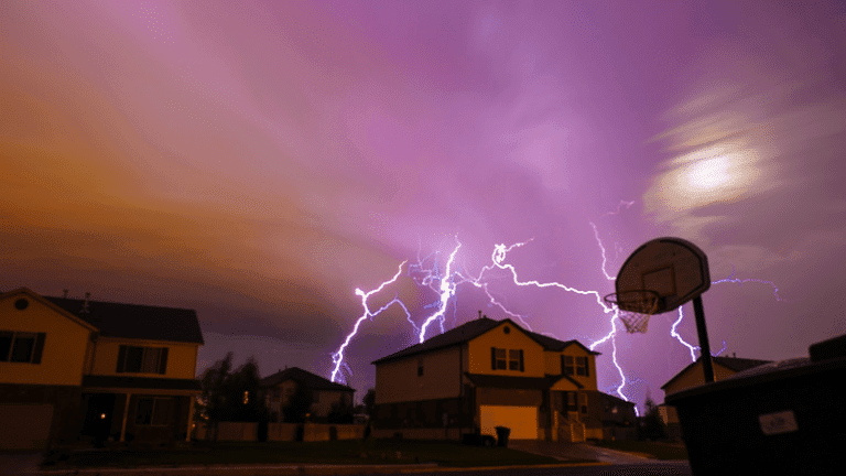 multiple lighting bolts striking behind a two-story home around dusk