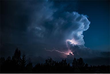 lightning strike in the sky behind clouds at night
